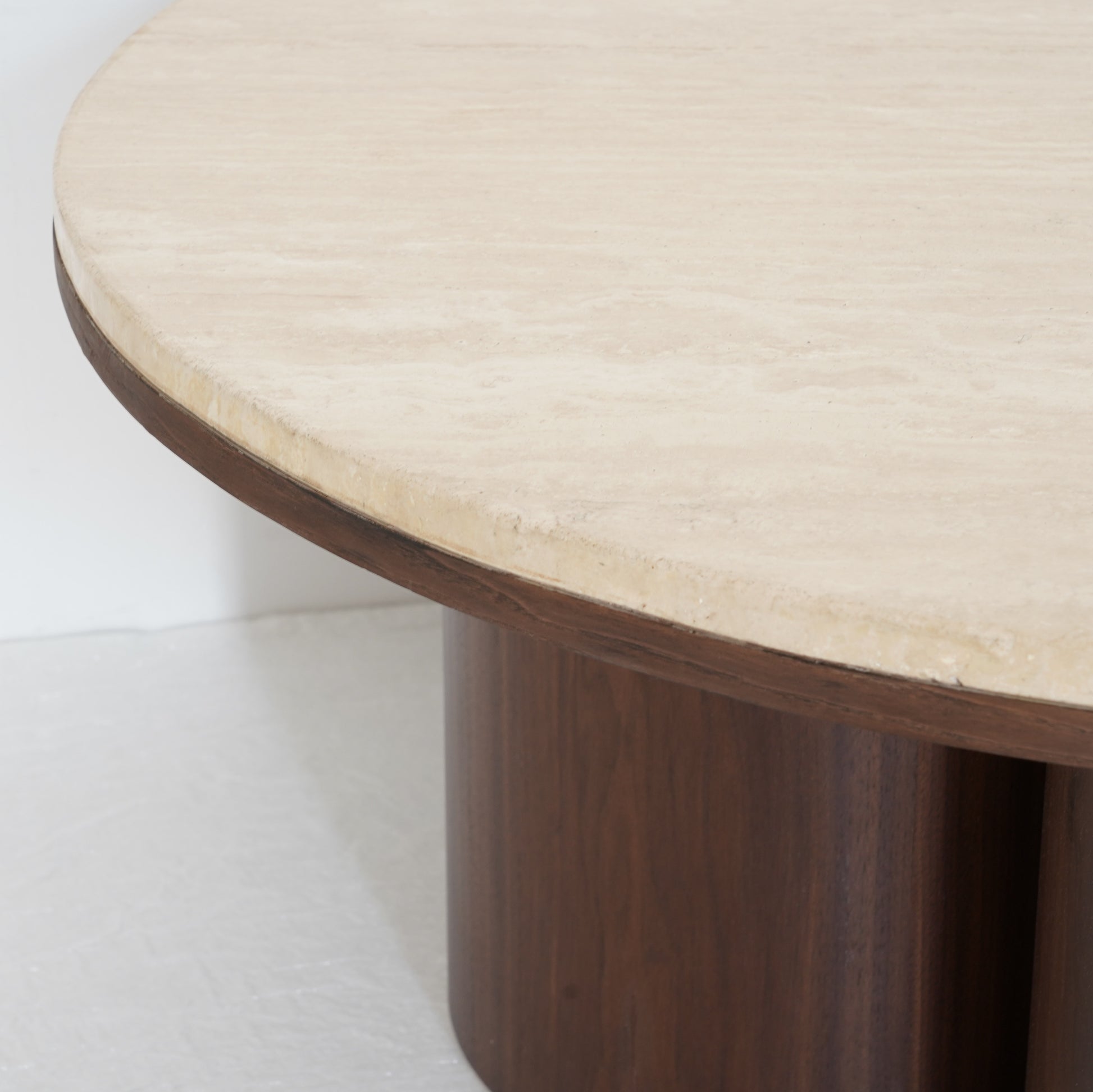 Round travertine coffee table with wooden legs, inspired by desert contours, styled in a contemporary living room.